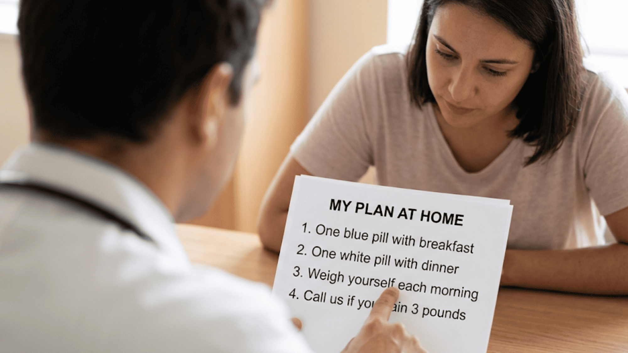 Clinician pointing to a printed take-home plan on a table while the patient reads along during a consultation