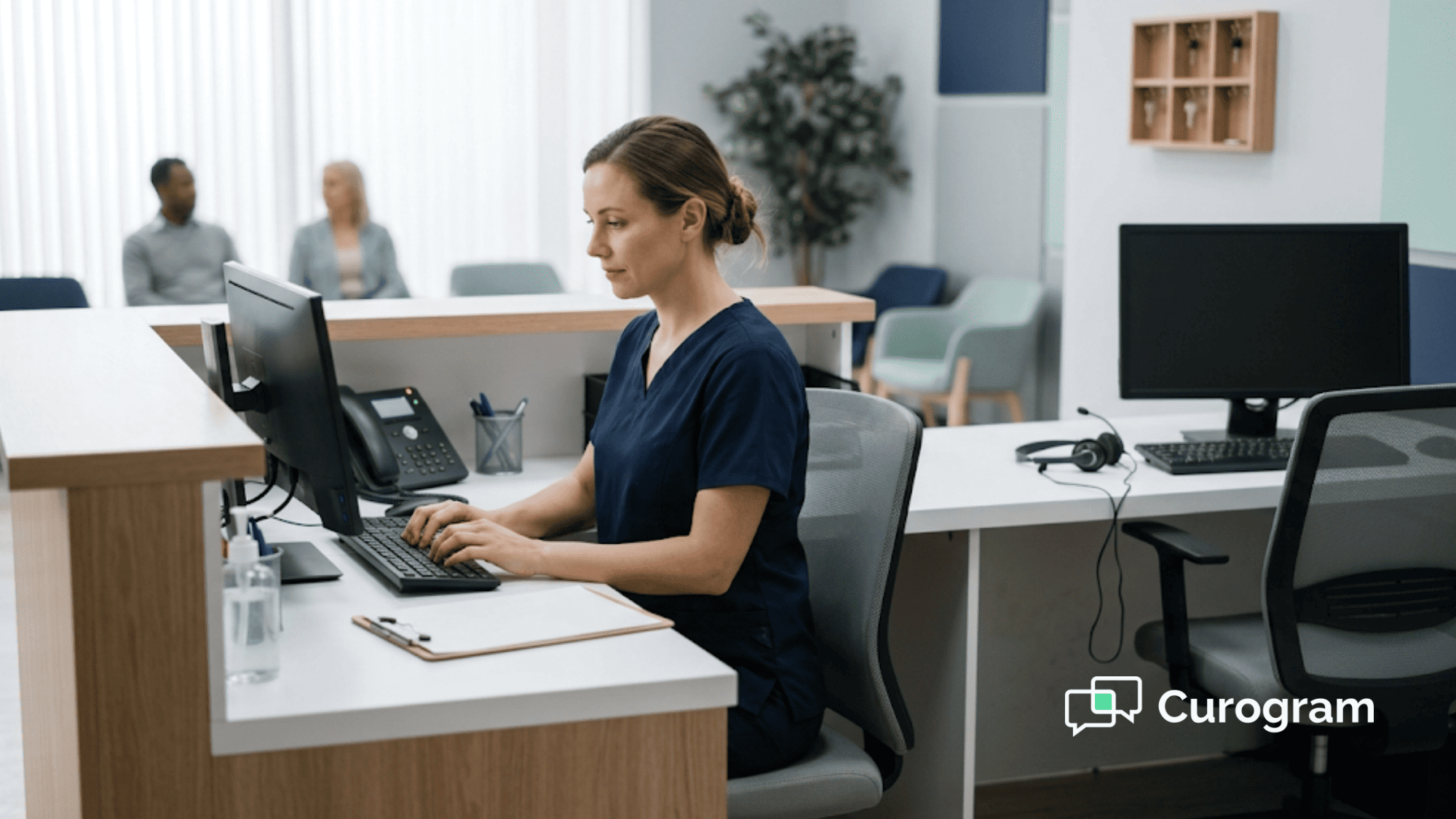 A clinic staff member types a reply to a patient text while a coworker's seat sits empty at a busy front desk