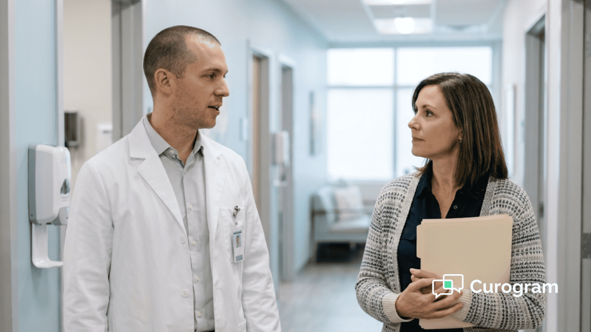 Physician assistant and office manager talking in a clinic hallway, one holding a closed folder