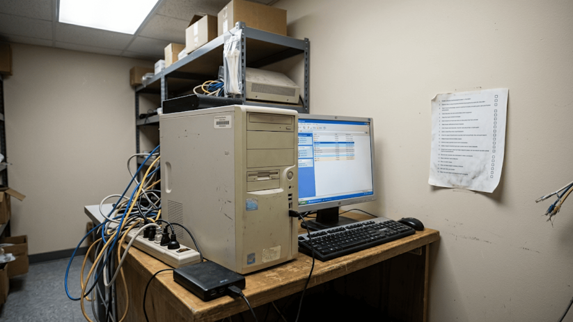 Legacy on-premise medical office server setup with older desktop tower ethernet cables and printed file transfer checklist pinned to wall