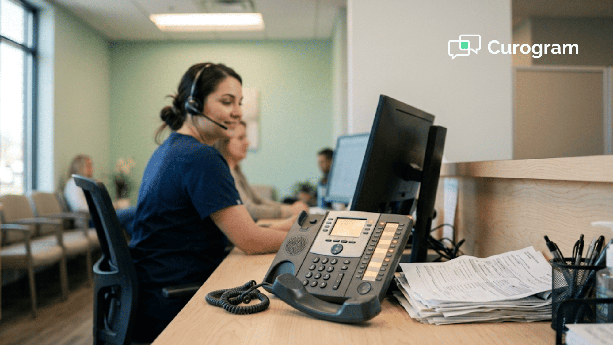 Clinic receptionist in a headset turning to greet a patient while four phone lines wait on hold