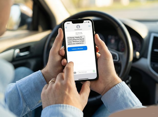 Close-up of hands holding a phone displaying an automated medical review request via text message