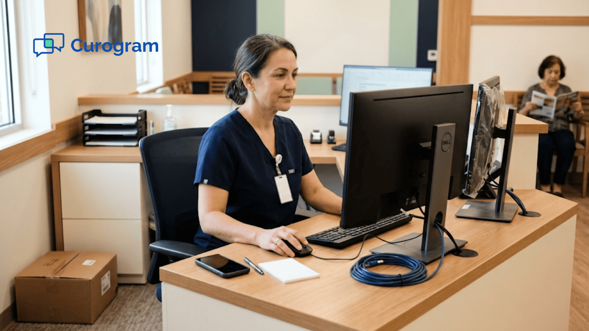 Medical assistant at a clinic front desk replies from the office computer while her personal phone lies face-down
