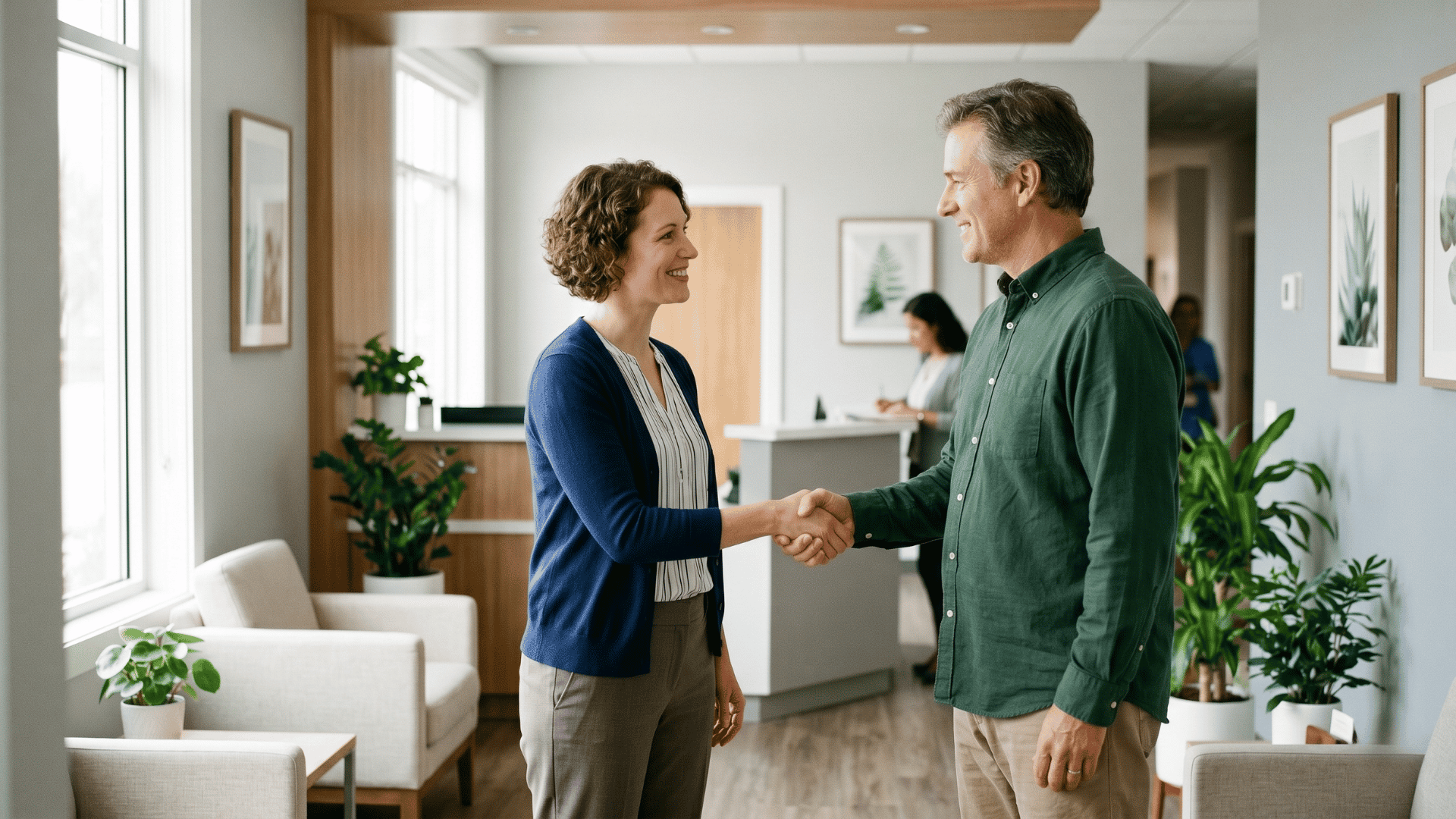 Behavioral health clinician warmly welcoming a returning client in a bright clinic lobby