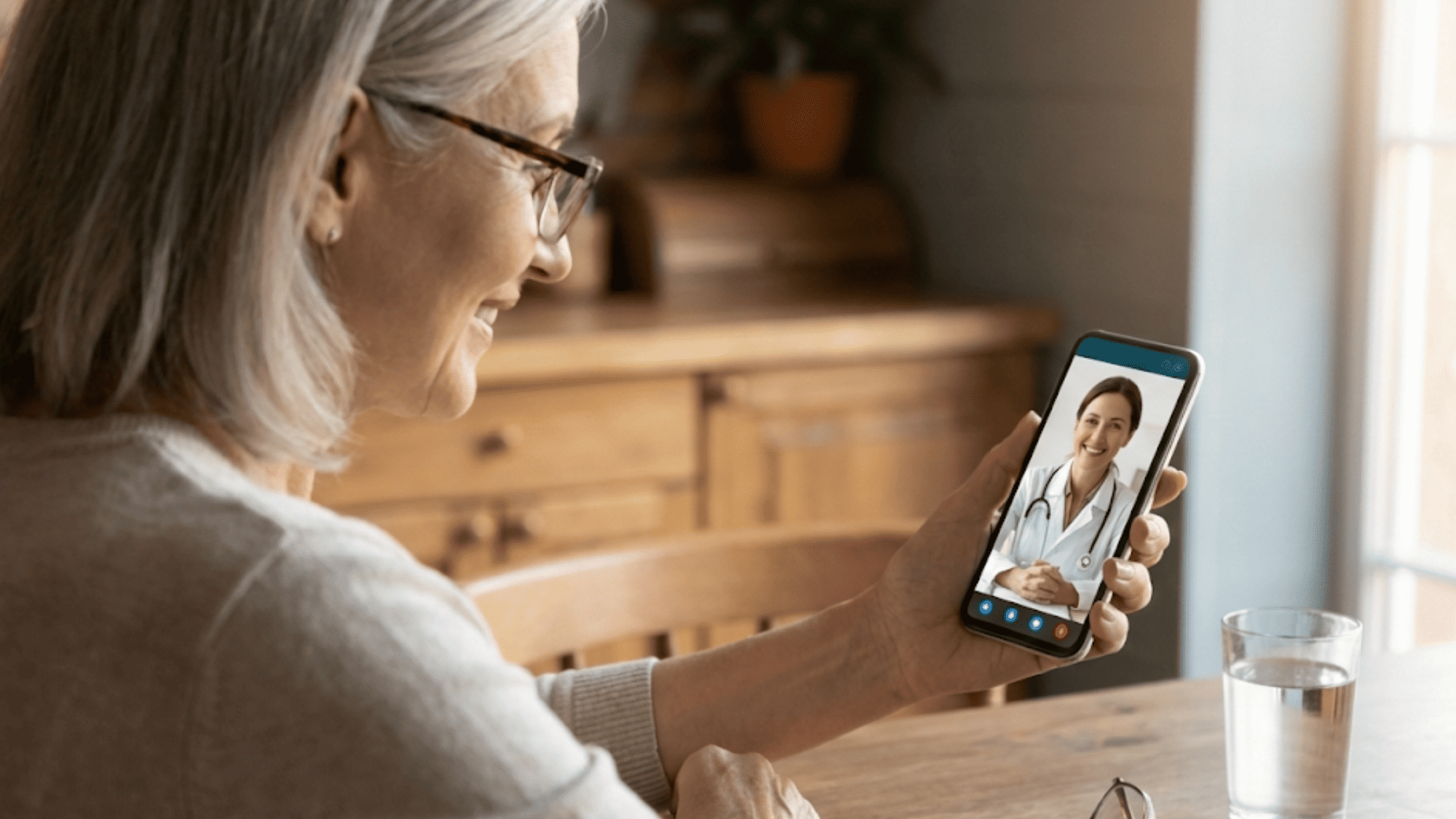 Older patient joining a telehealth visit on her smartphone from her kitchen table