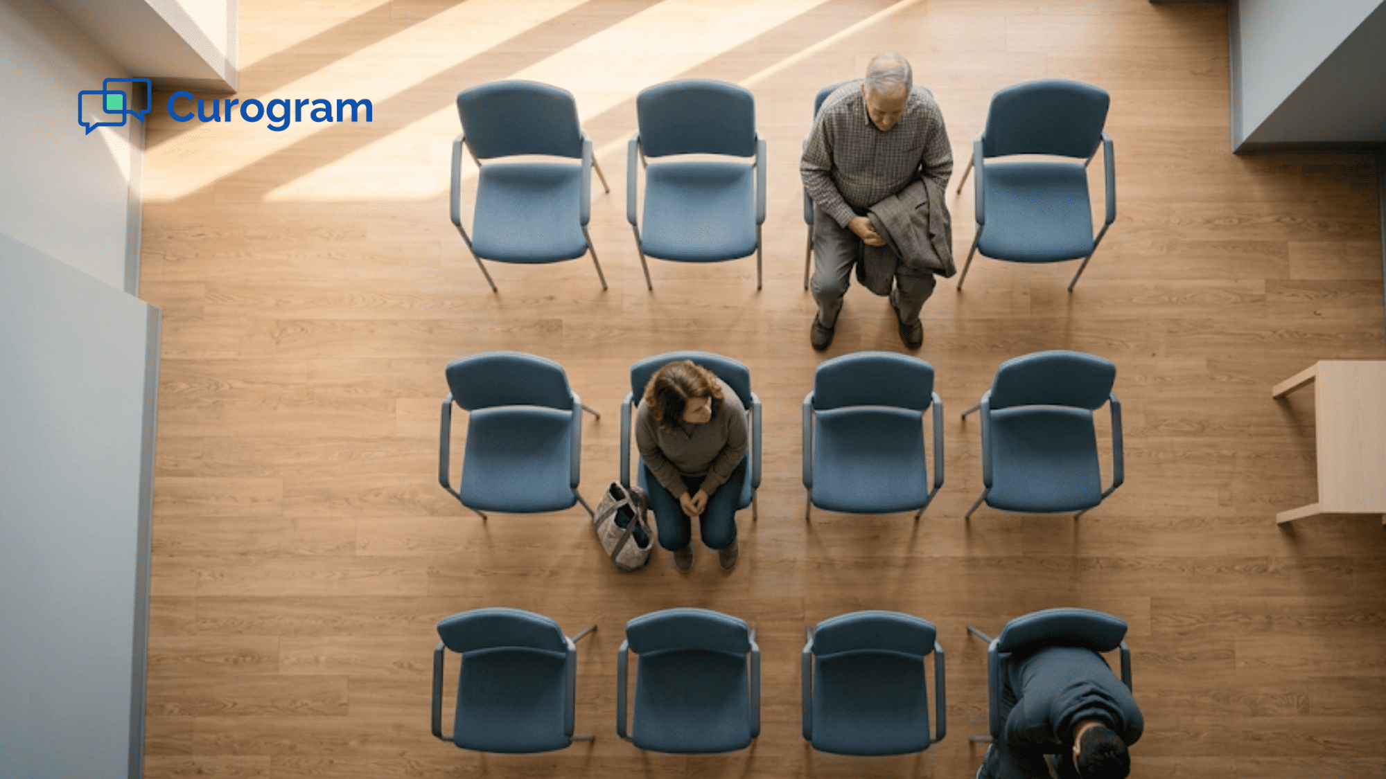 Overhead view of a clinic waiting room with three patients seated and most chairs empty