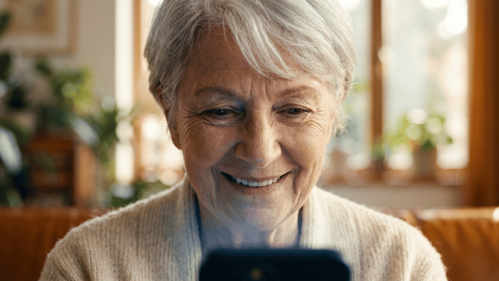 Elderly patient smiles at her phone during a text-link video visit, showing how easy telehealth can be.