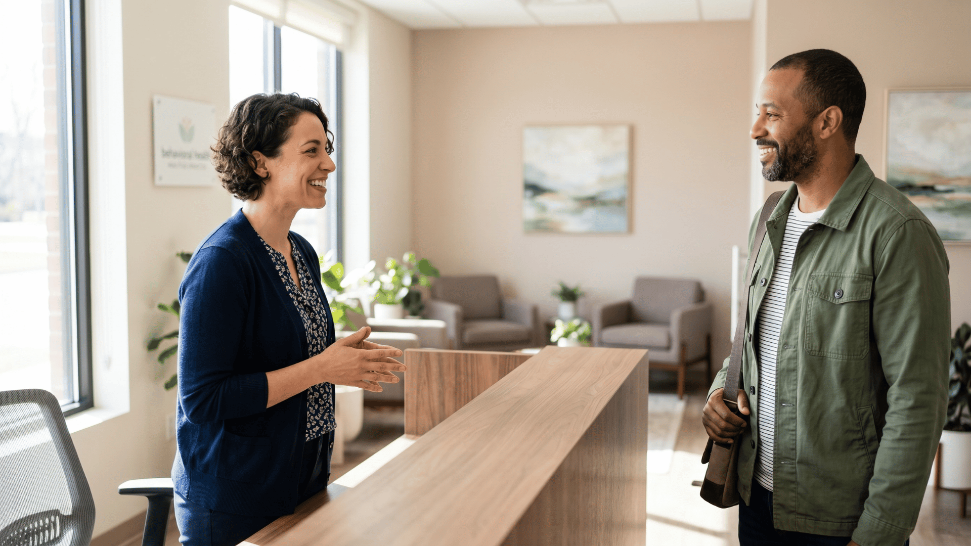 Front desk coordinator warmly greeting an arriving behavioral health client without paperwork