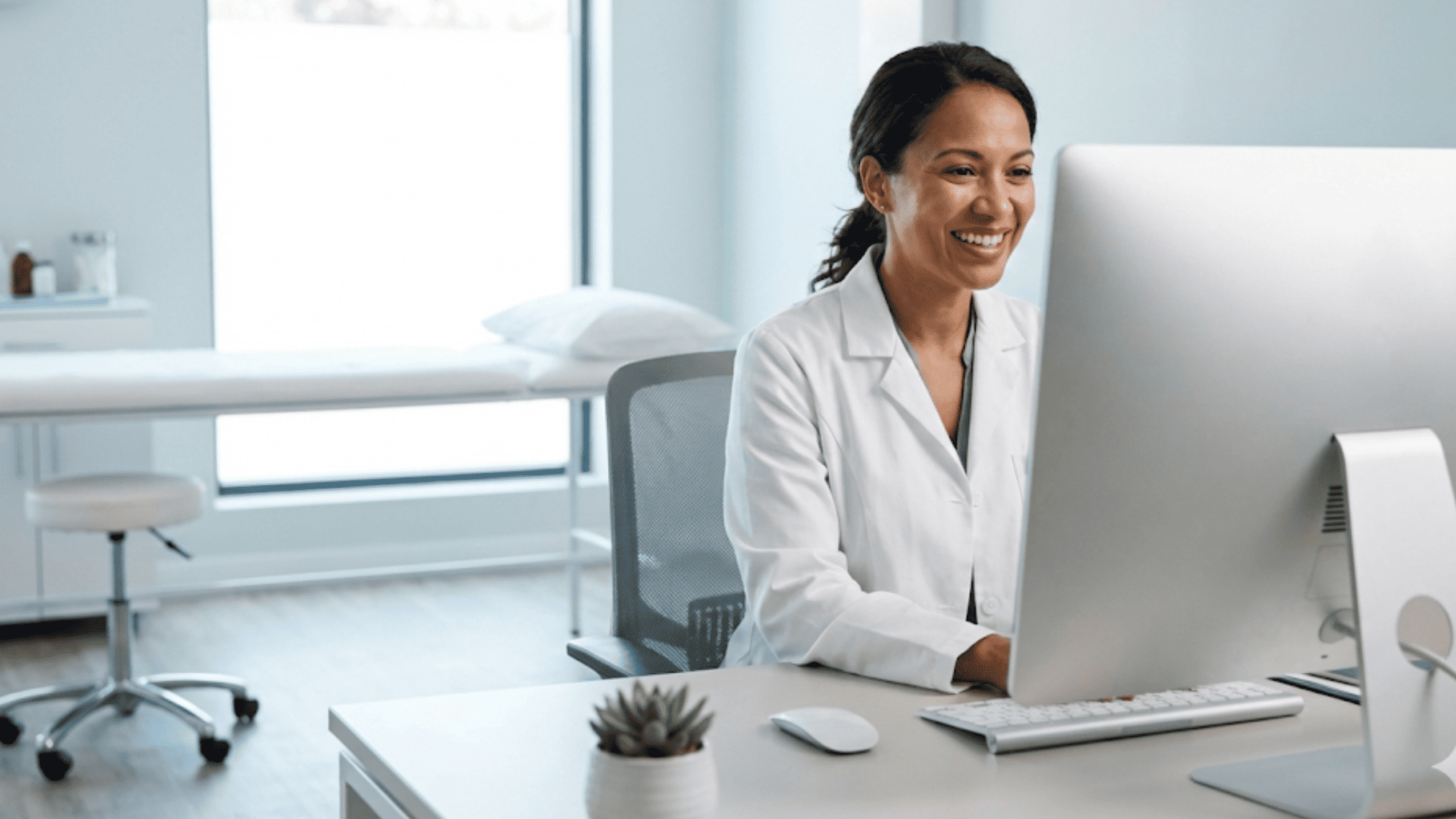 Smiling doctor conducting a telehealth video visit from a modern exam room