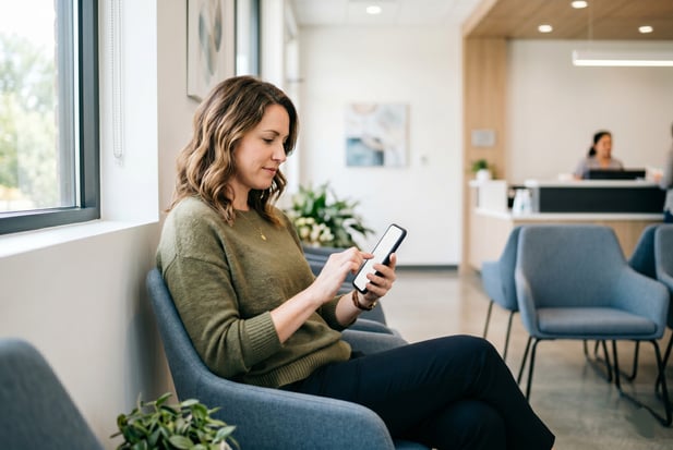 Seated patient uses a smartphone to complete pre-appointment forms in modern waiting area