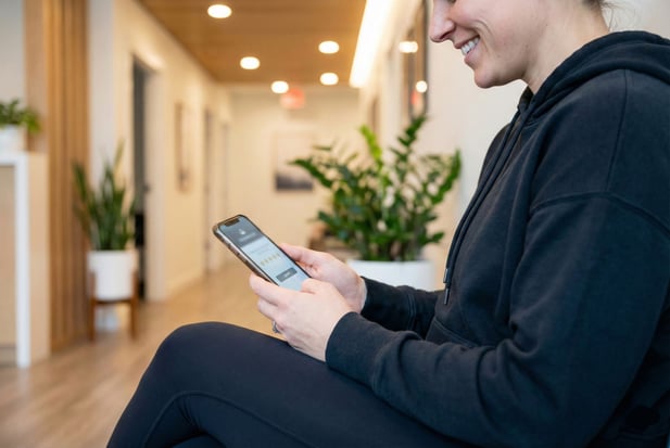 Smiling physical therapy patient in a waiting area, looking at a review prompt on her phone