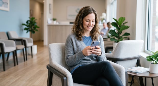 Satisfied healthcare patient in modern waiting room using their smartphone