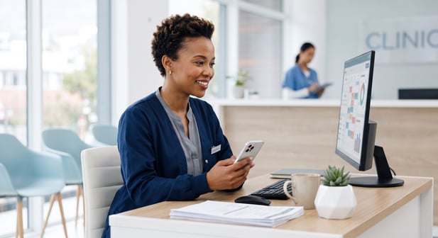 Smiling medical practice manager using a smartphone to manage a modern clinic scheduling dashboard