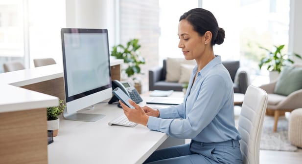 Professional receptionist using a smartphone at a modern office desk
