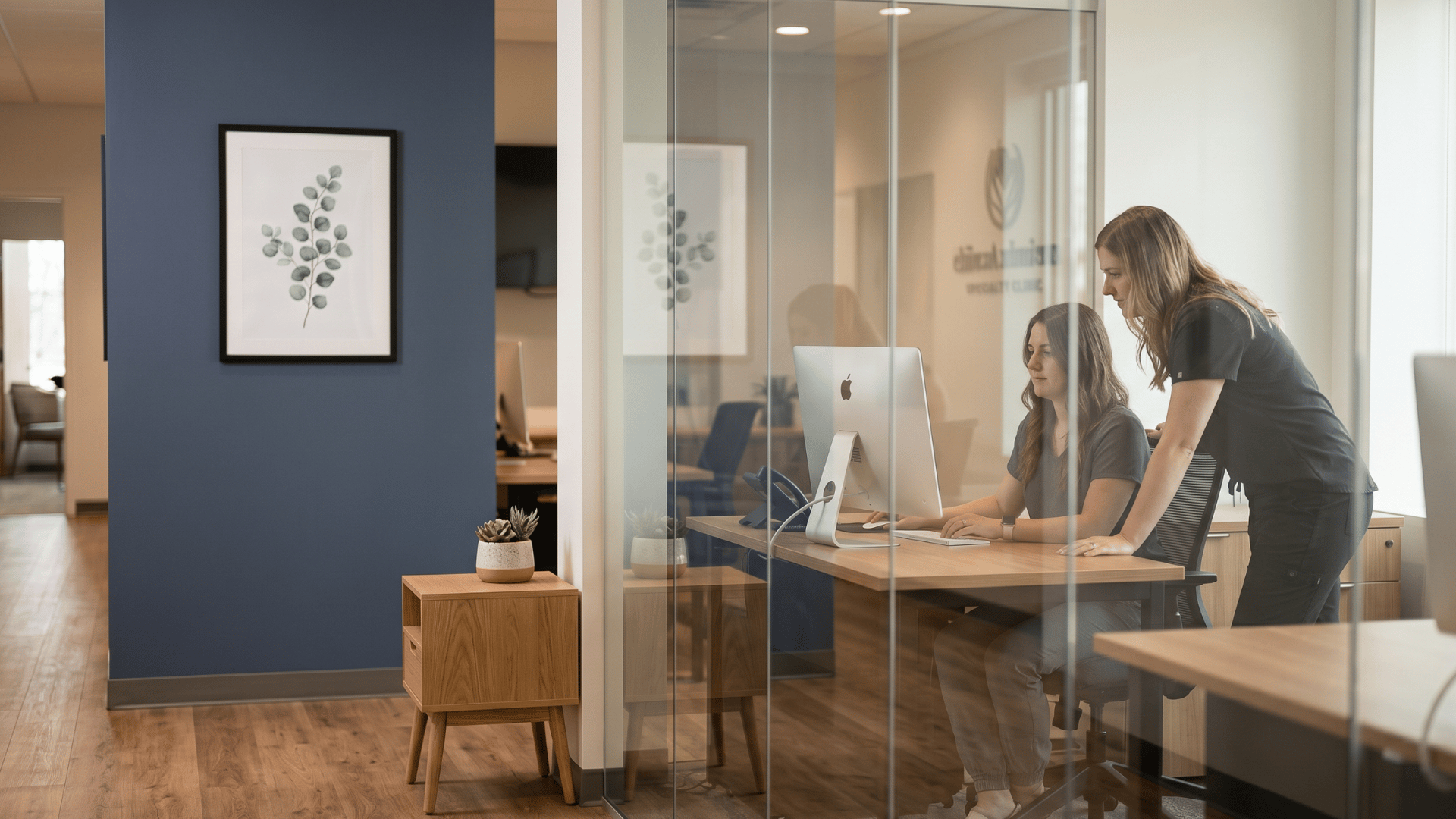 Two clinic coordinators collaborating at a shared workstation inside a modern Modmed specialty practice