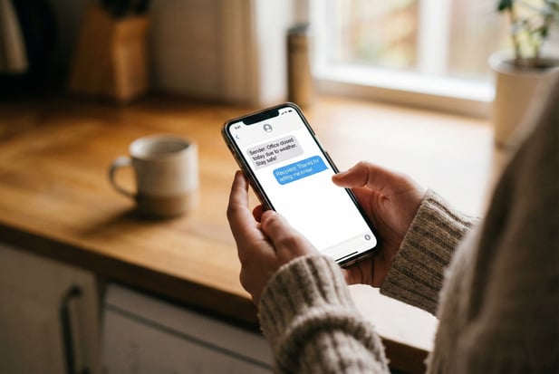Close-up of hands sending a patient office closure text message from a smartphone