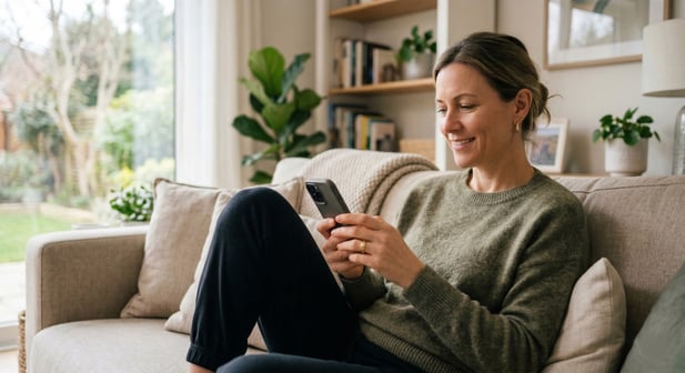 Smiling woman using her smartphone comfortably on a couch, suggesting telehealth ease