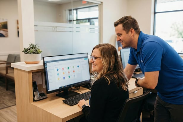 Clinic front desk staff reviewing patient appointment scheduling software on a computer together