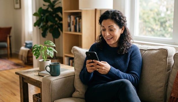 Woman on couch pleasantly surprised, reading a text message from her medical office