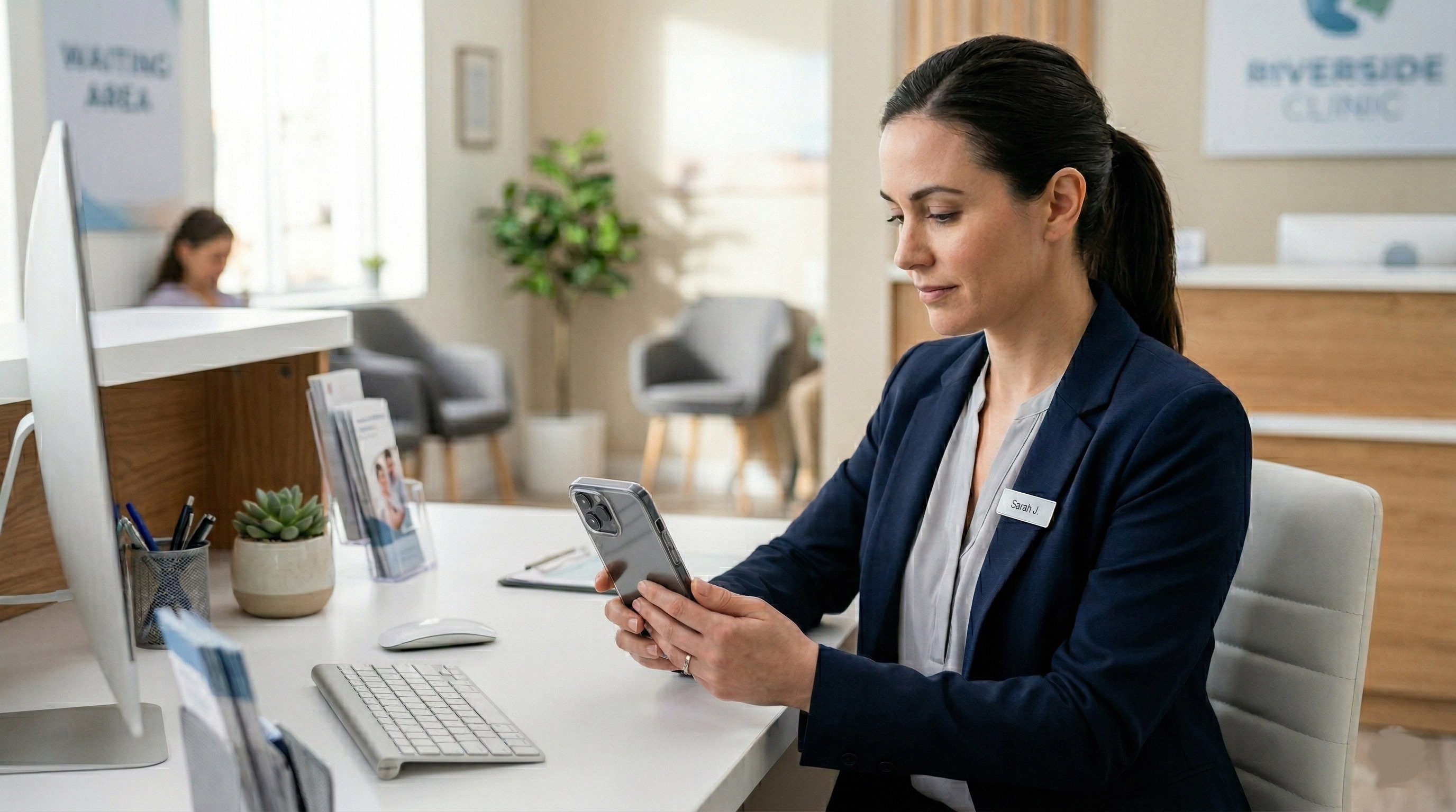 A medical receptionist at a modern clinic desk, managing communications on a smartphone