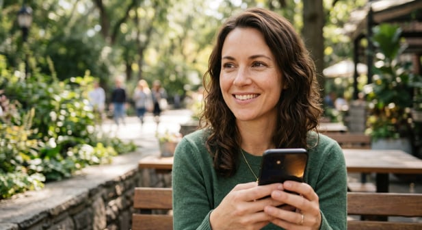Candid close-up of an adult holding a smartphone outdoors with a calm, hopeful expression