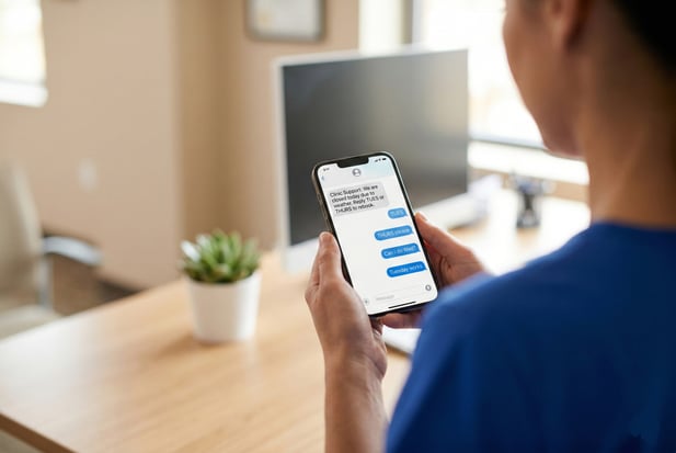 Close-up of healthcare staff holding a smartphone displaying clinic SMS rebooking messages