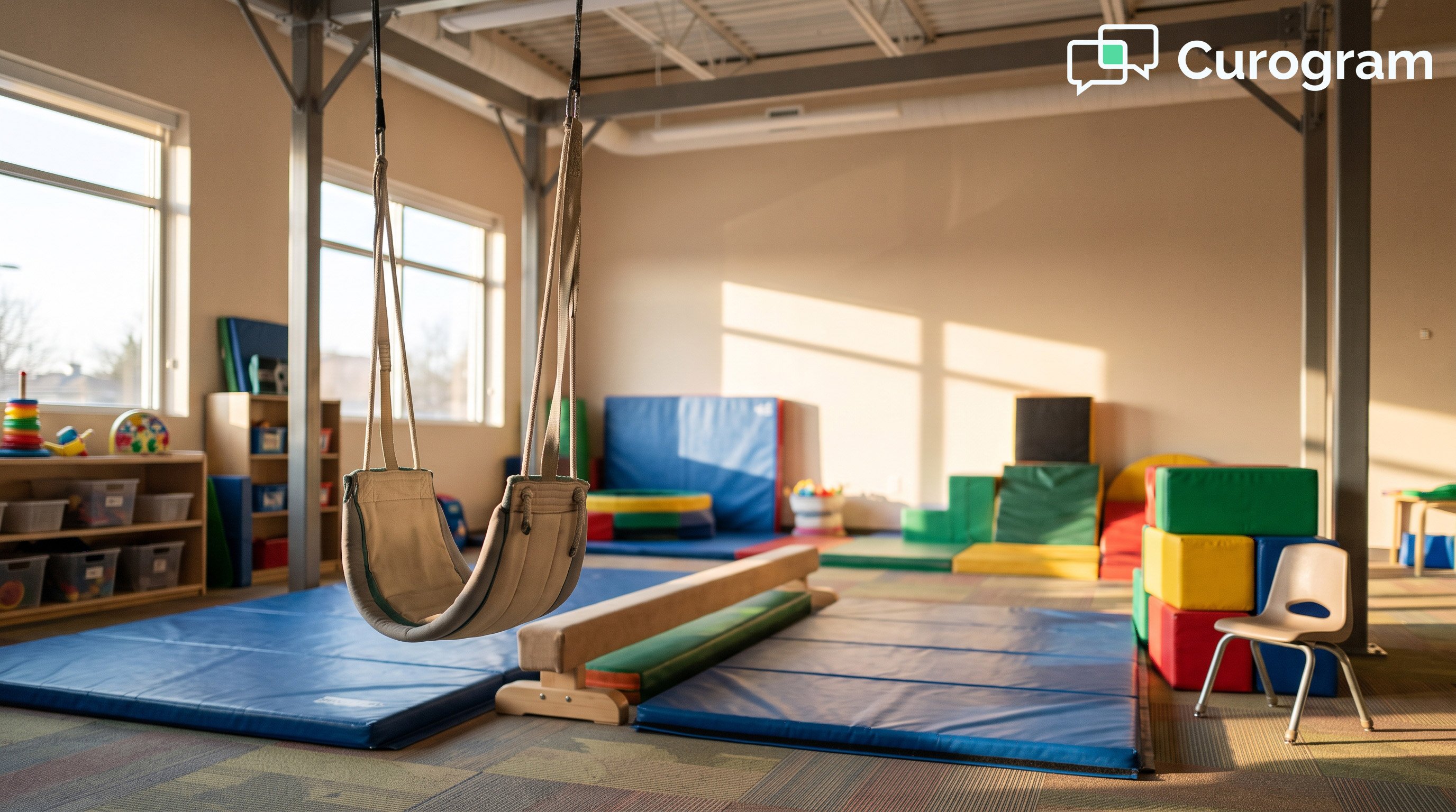An empty pediatric therapy gym with a still therapy swing, foam blocks, and a small chair waiting beside a floor mat