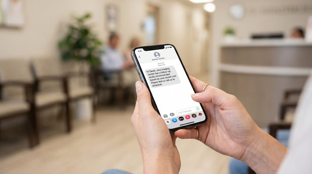 Patient in medical office waiting room reading appointment reminder text on phone